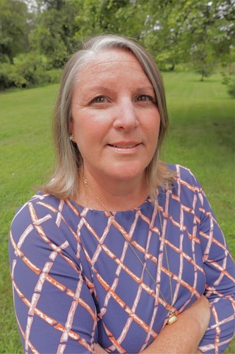 White woman standing in front of a field of green grass.