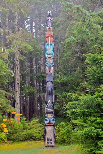Totem pole painted in traditional colors-red, blue-green, and black-with figures of men, animals, and the moon.