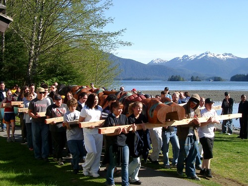 People carrying a totem pole on lumber.