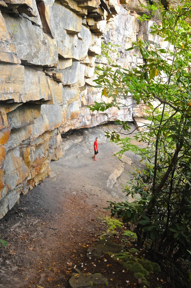 hiker standing beneath large cliff