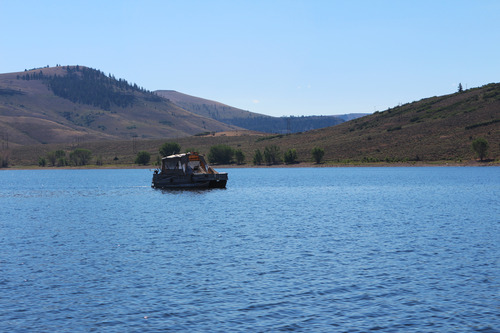 A small, covered boat floats along a flat body of water. There are mesas in the background.