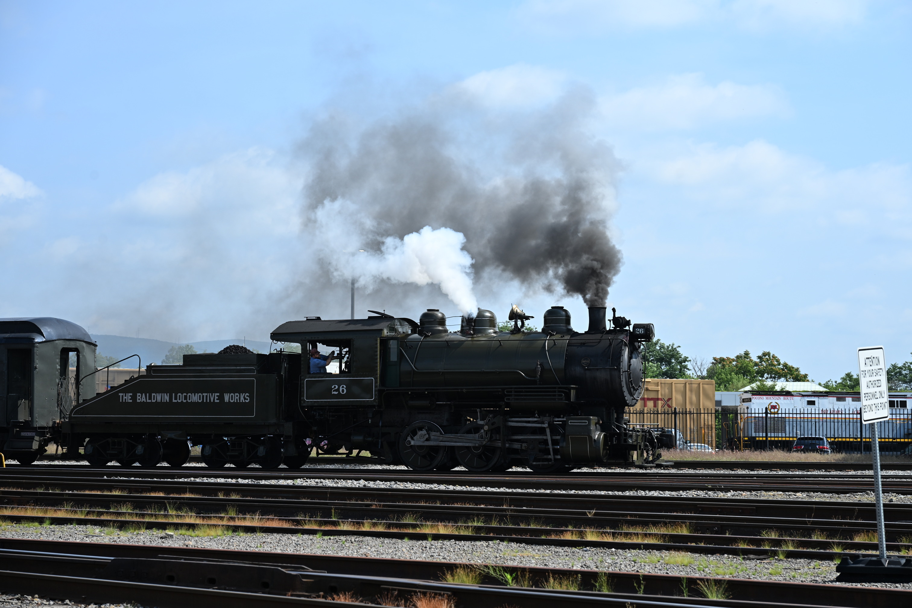 Steam Locomotive puffing white and dark gray smoke and moving along the tracks. 