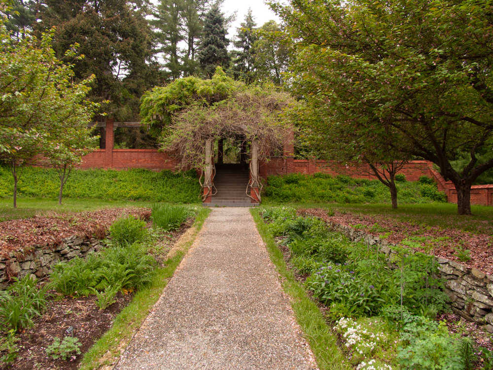 A gravel path flanked by flowering plants terminating in a brick pergola.