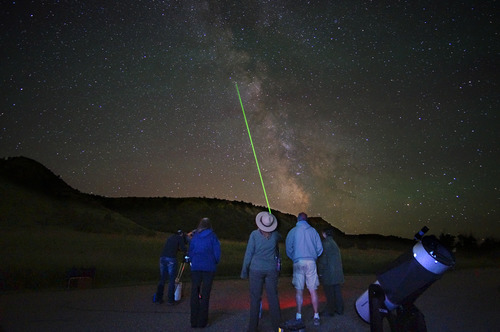 A Park Ranger pointing a green laser into the Milky Way night sky while a group of people look on.