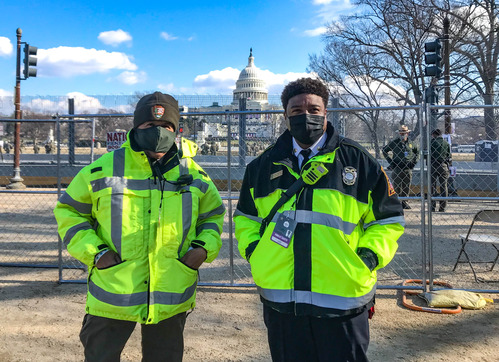 A National Park Service employee and D.C. government employee standing next to a fence with the U.S. Capitol building in the background 