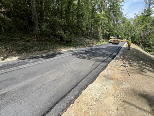 Construction equipment and workers paving the road at milepost 224.9 with the slope that was recently rebuilt in the foreground with a layer of fill dirt on top. 