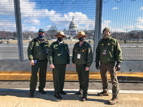 Four National Park Service employees standing next to a fence with the U.S. Capitol building in the background 