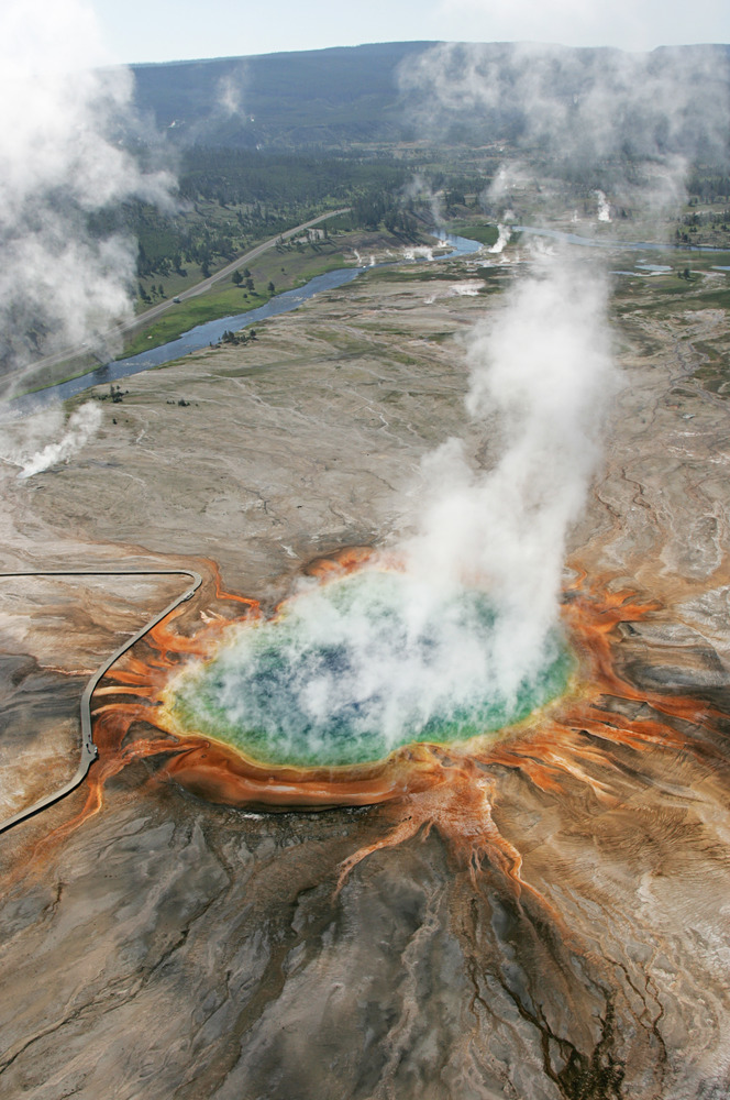 Looking down on a huge blue hot spring with orange bacteria mats surrounding it.