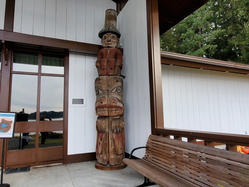 A totem pole fragment. Northwest coast stylized Bear with a Human wearing a tall hat on top. Black , blue and red paint is is very worn or weathered.