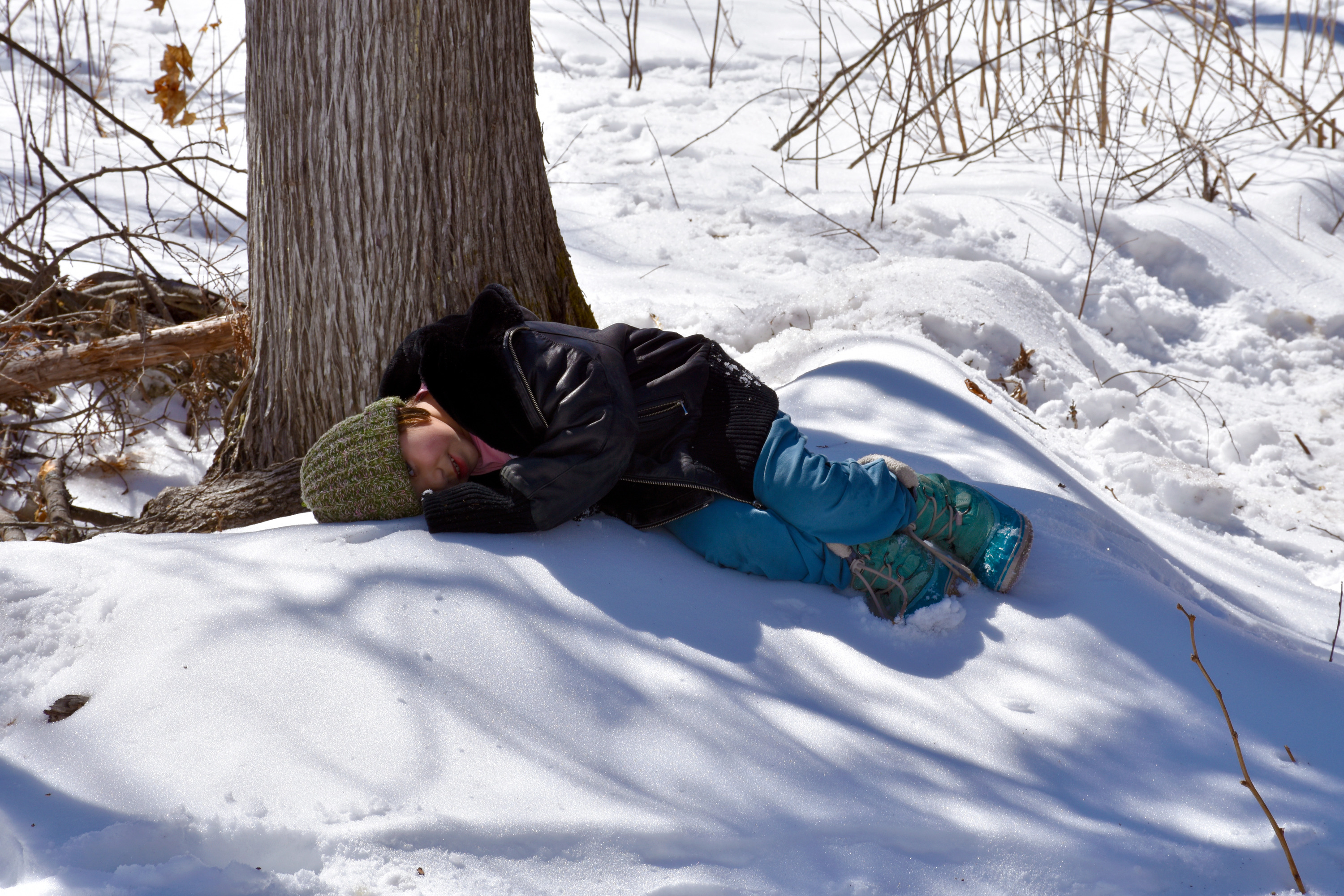 A child lies on a snowdrift under a tree.