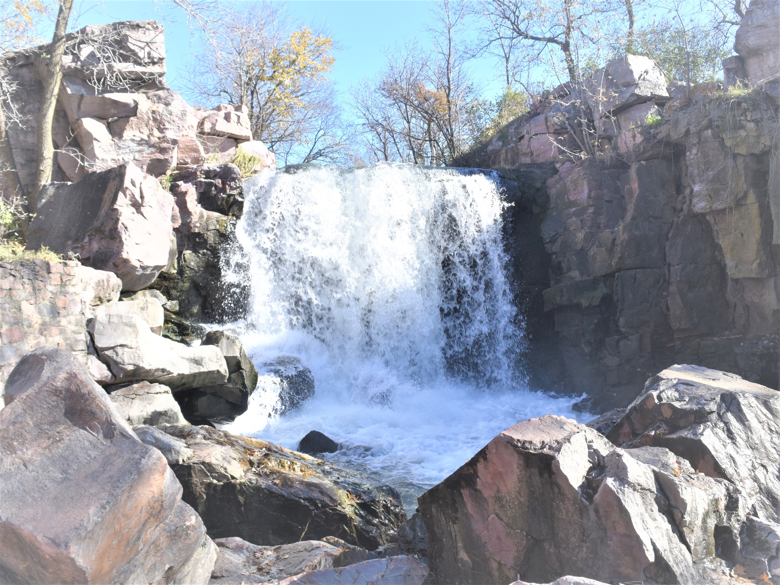 Waterfall underneath a blue sky and surrounded by quartzite cliffs and boulders.