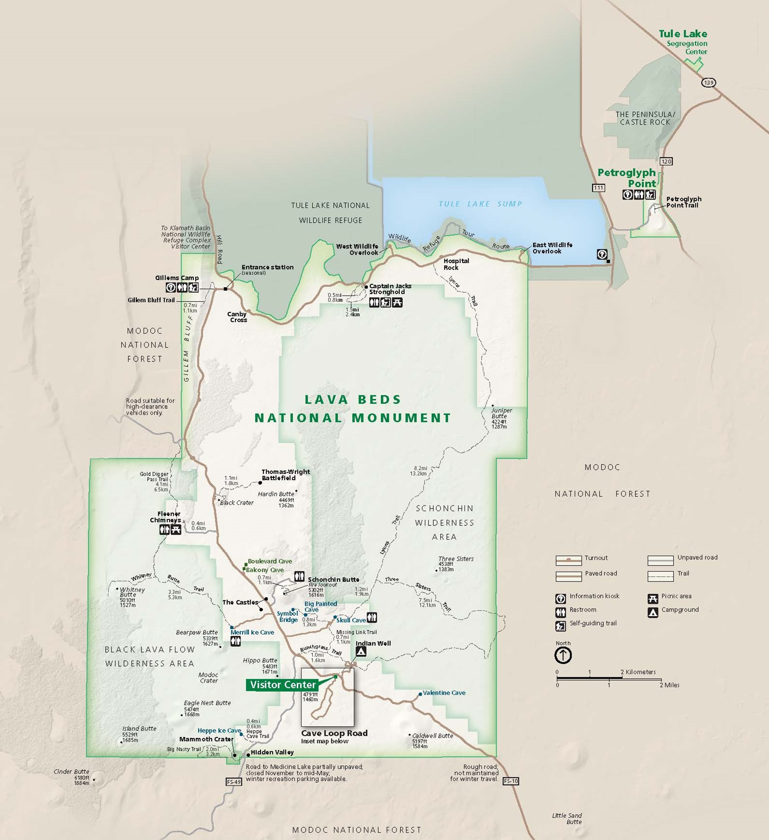 Map of Lava Beds National Monument in California. Represented in green, the park’s border is dark green with areas of white and pale green within the boundary. Dozens of named rivers, buttes, peaks, caves, trails, and other features are labeled.