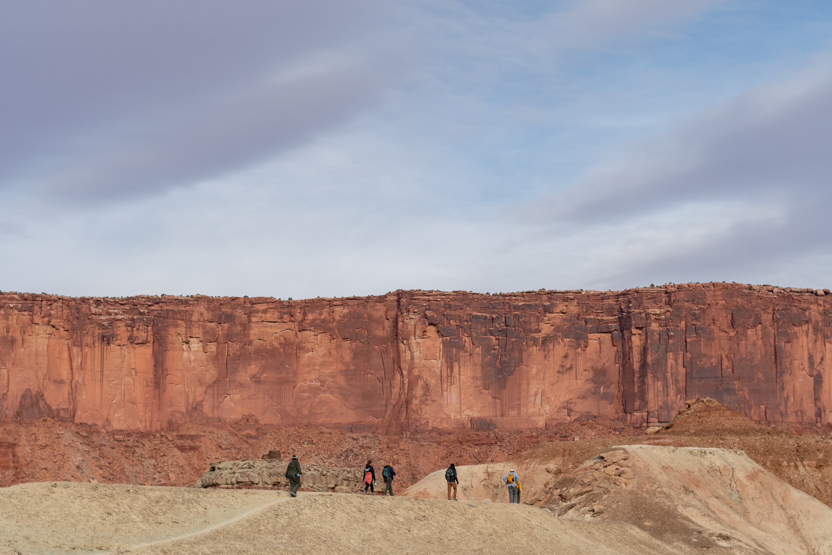 Five people walking along a trail with canyon walls in the background