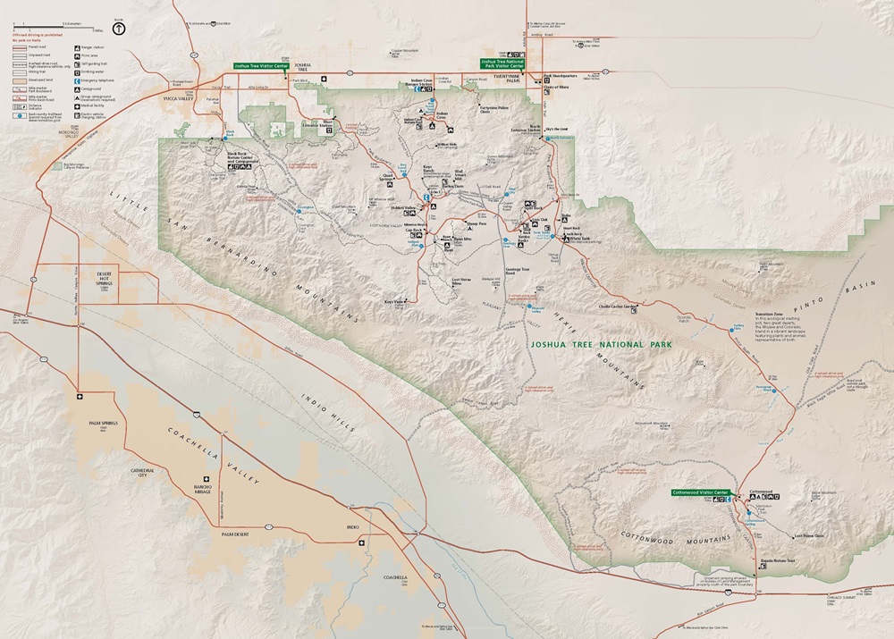 Map of Joshua Tree National Park in California. The park is roughly trapezoidal in shape and is shaded tan with a green border, and it stretches nearly the full width of the map. Surrounding land is shown in lighter beige, roads are represented by orange lines, and trails are shown with dashed black lines.