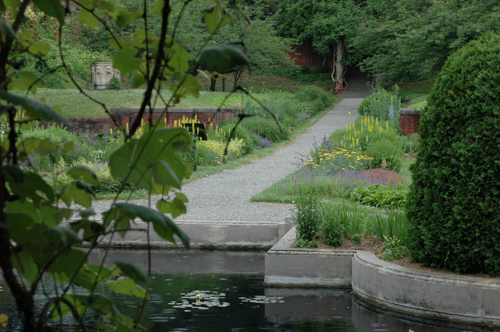 A flowering garden with reflecting pool in the foreground and a gravel path leading toward a pergola.
