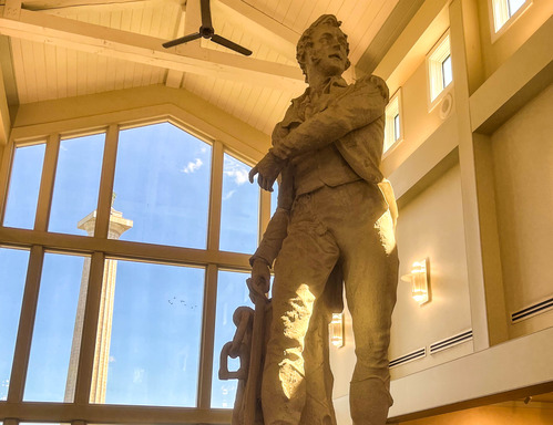 Statue of statue of Oliver Hazard Perry with the memorial column visible outside the window