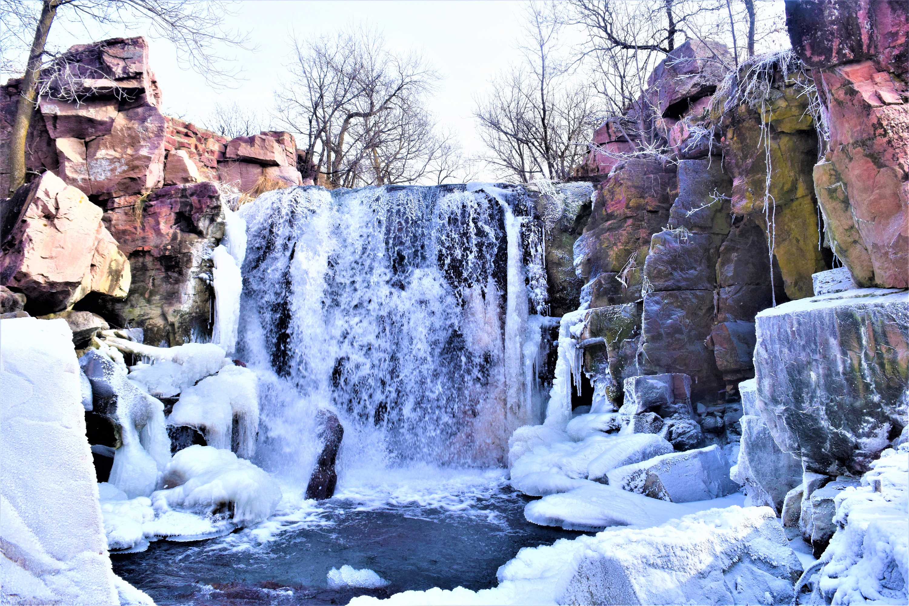 Waterfall surrounded by pink cliffs and snow.