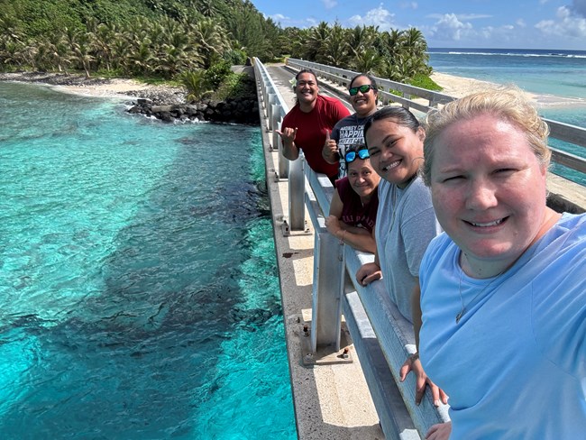 Outdoors; group of young women facing camera on bridge with blue water below and an island behind.