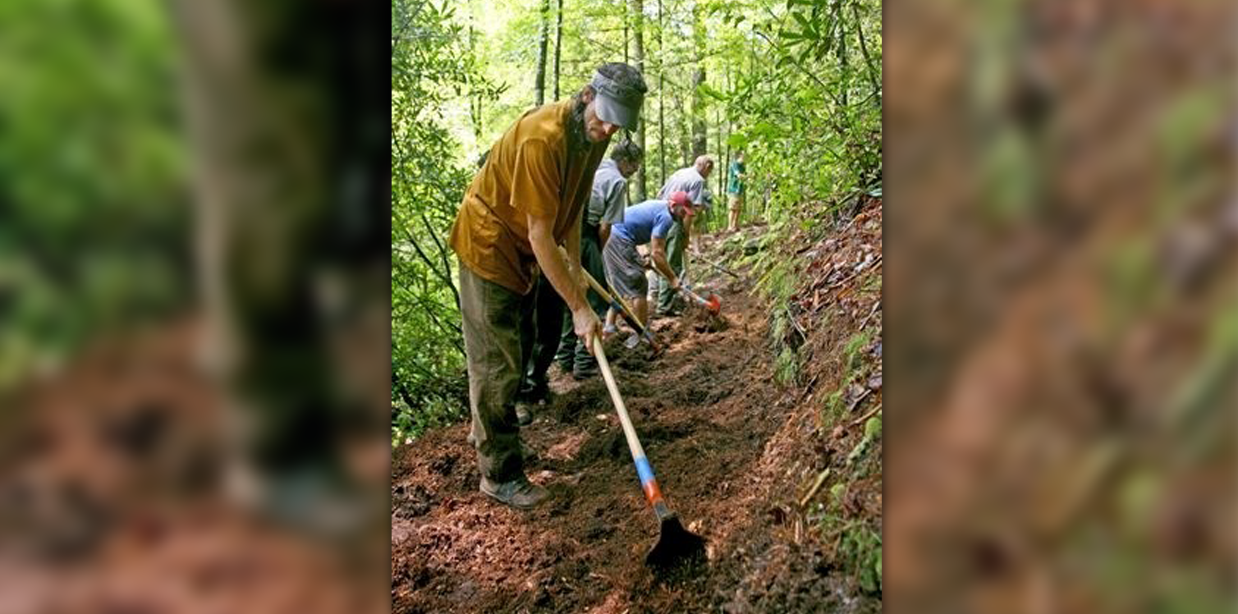 A man in the front with a tool working on a trail.