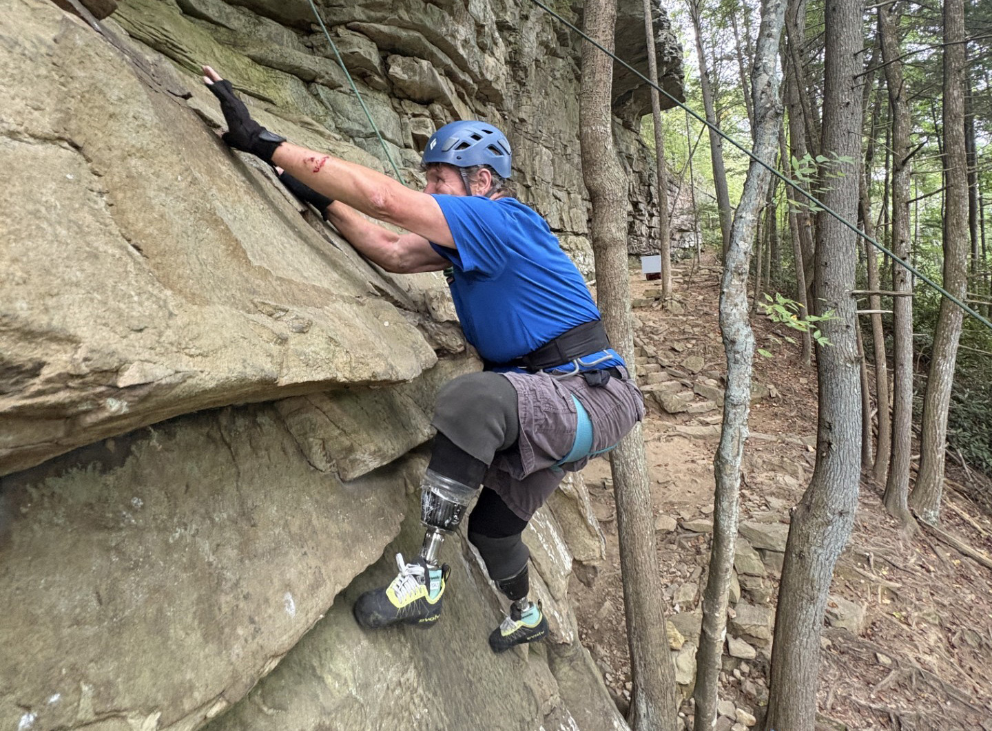 A male adaptive climber climbs up a rocky cliff.