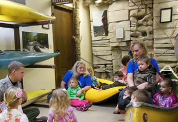 Little children sitting on floor around a park ranger who is telling a story