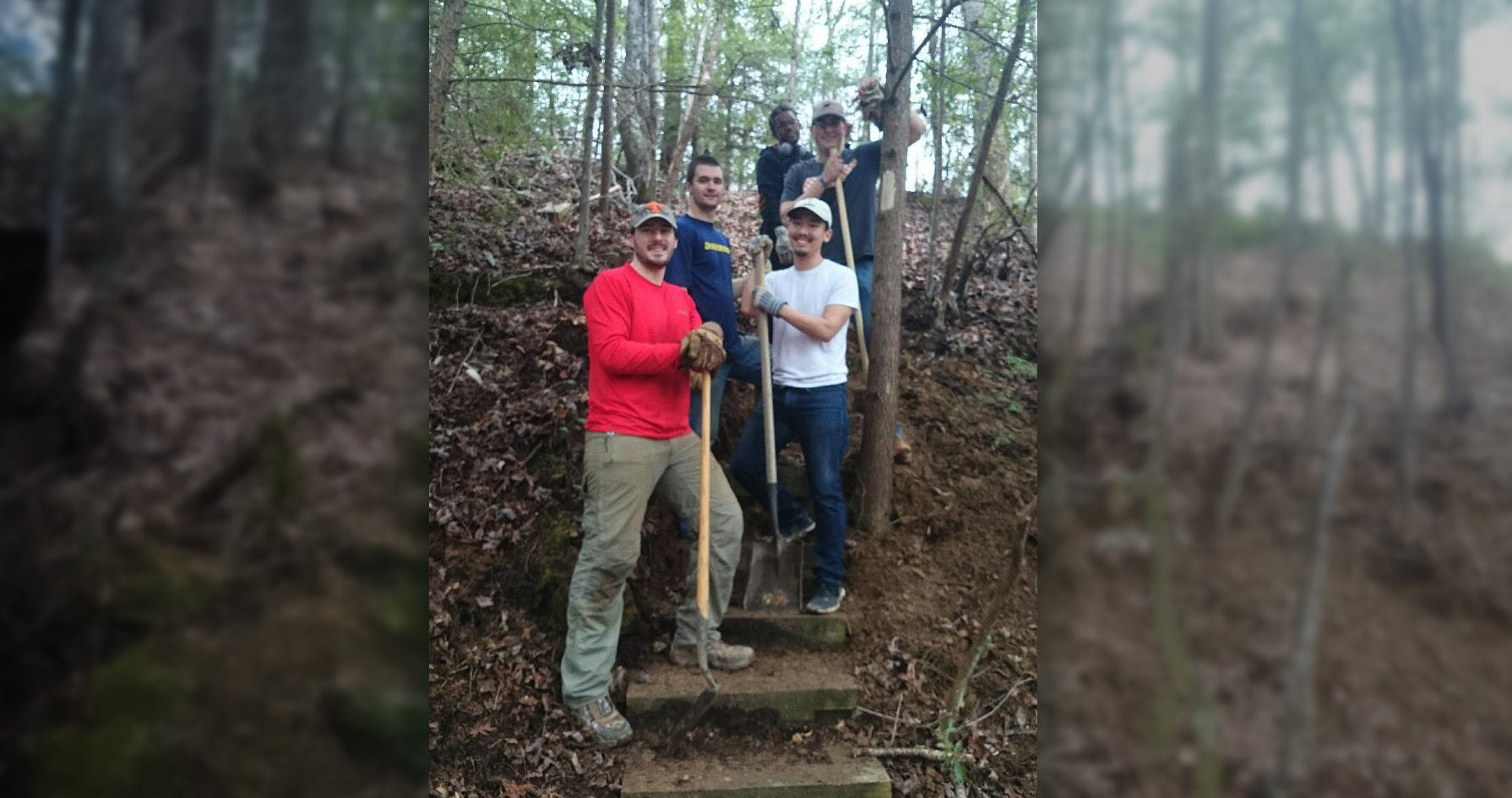 A group of people standing on stairs on a trail holding shovels.