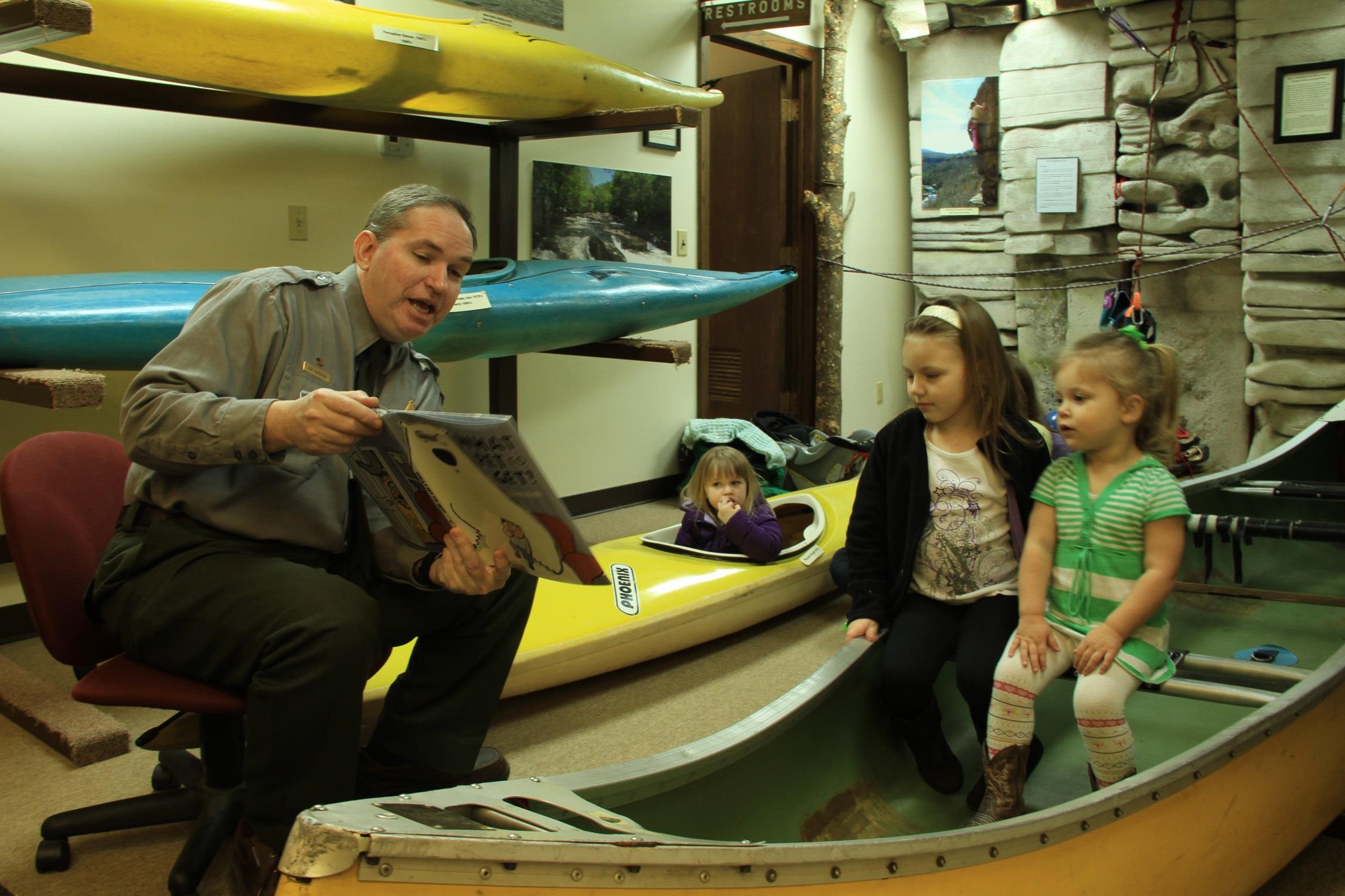 Ranger Joe reading to two little girls sitting in a yellow canoe