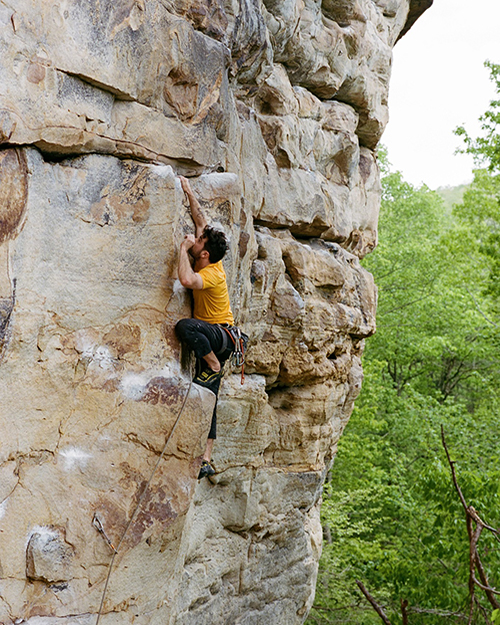 Climber scaling a steep cliff face, reaching out for the next handhold.