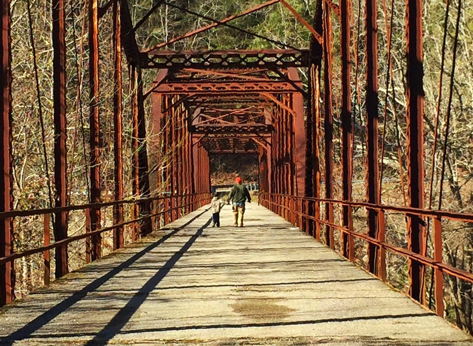 father holding little son's hand while walking across red colored rusty bridge father holding little son's hand while walking across red colored rusty bridge