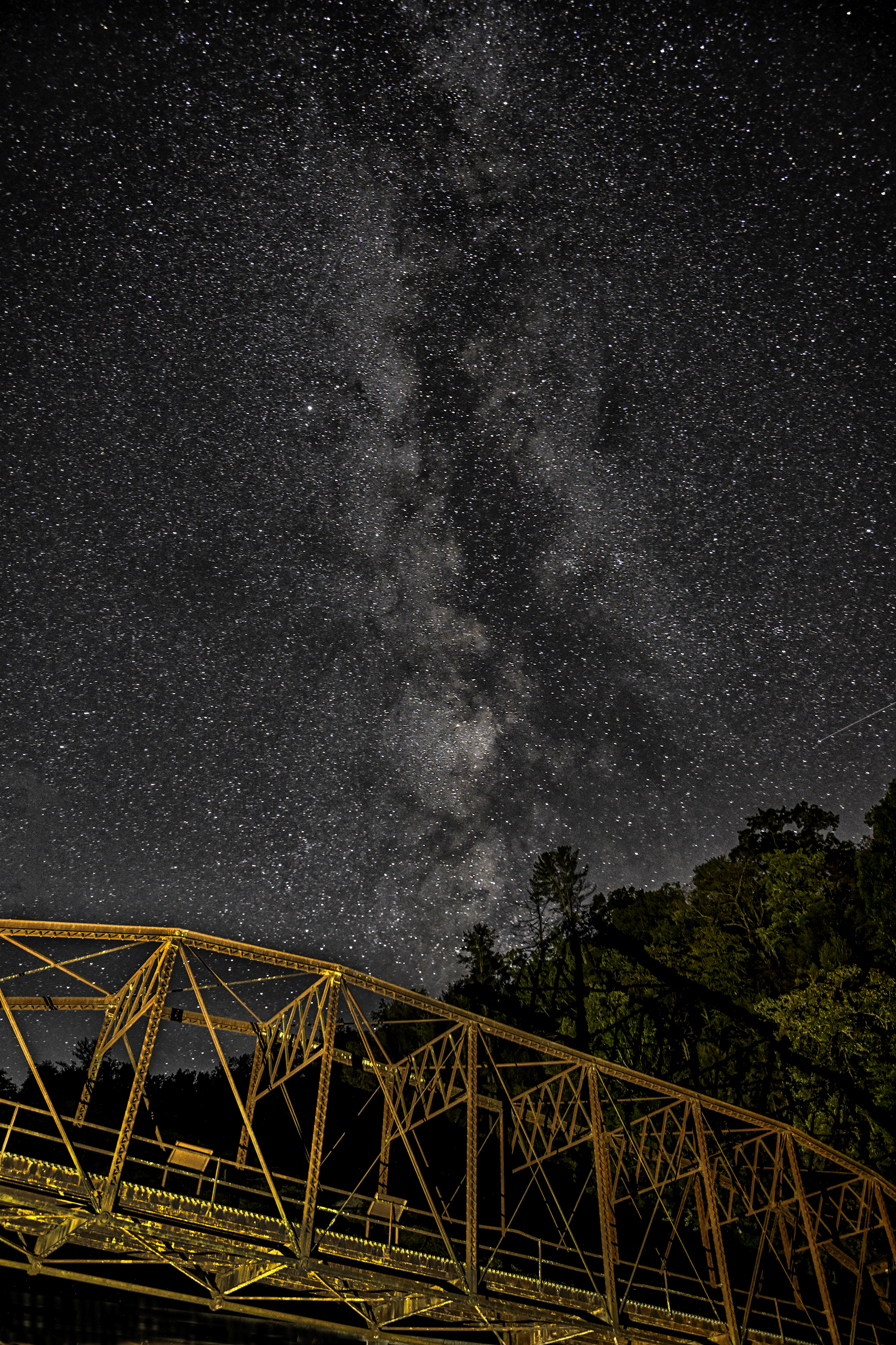 A starry Milky Way over an iron truss bridge