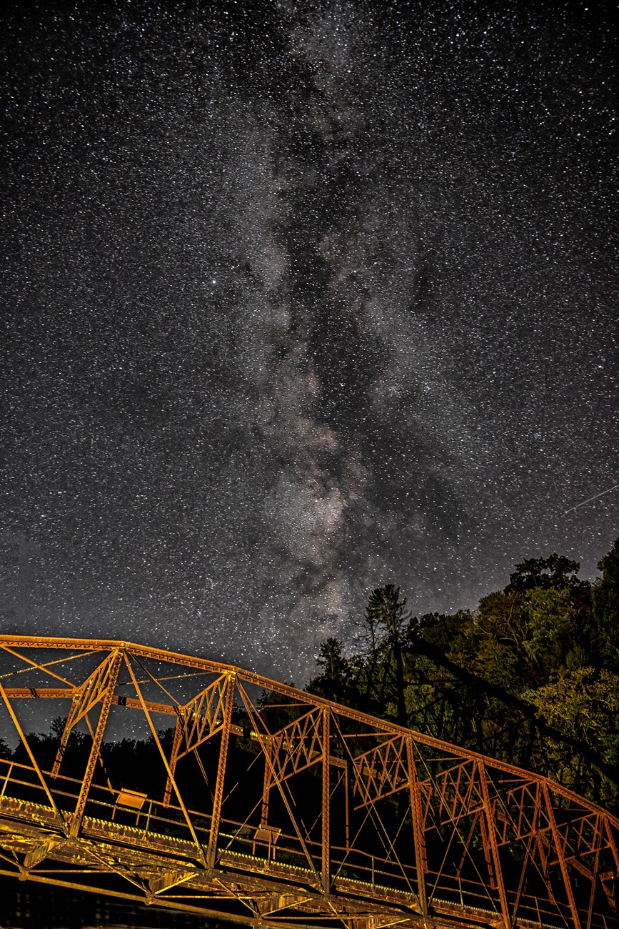 A starry Milky Way over an iron truss bridge