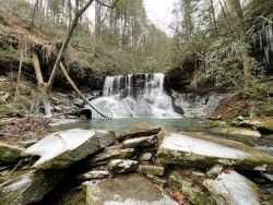 Waterfall surrounded by large rocks and trees.