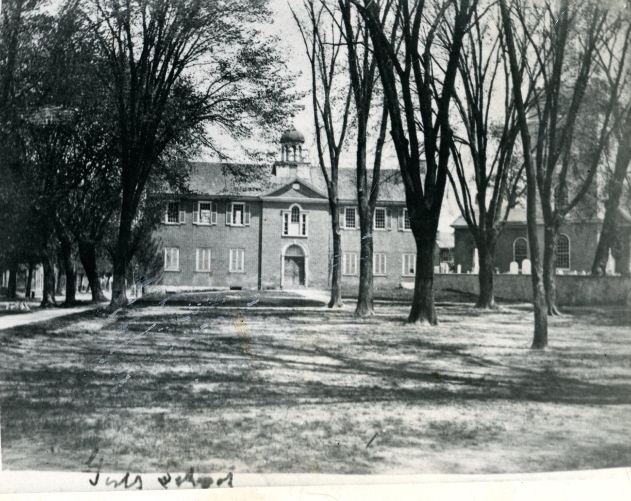 A two story colonial brick building with trees in front of the building.
