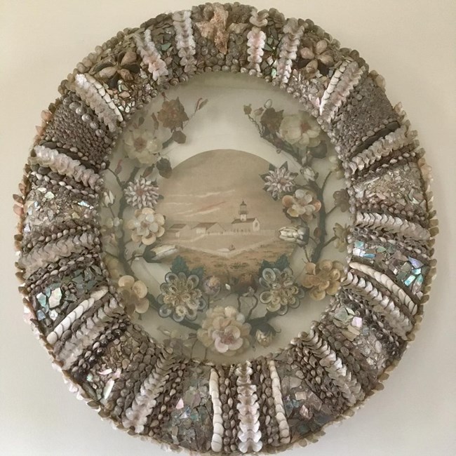 Shell artwork created by Maria Arcadia Israel An image of a round shell artwork with flowers wrapped around a view of buildings and a grassy field.