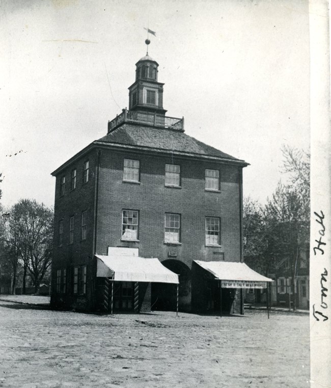 Three story square brick building with an arched tunnel in the middle.