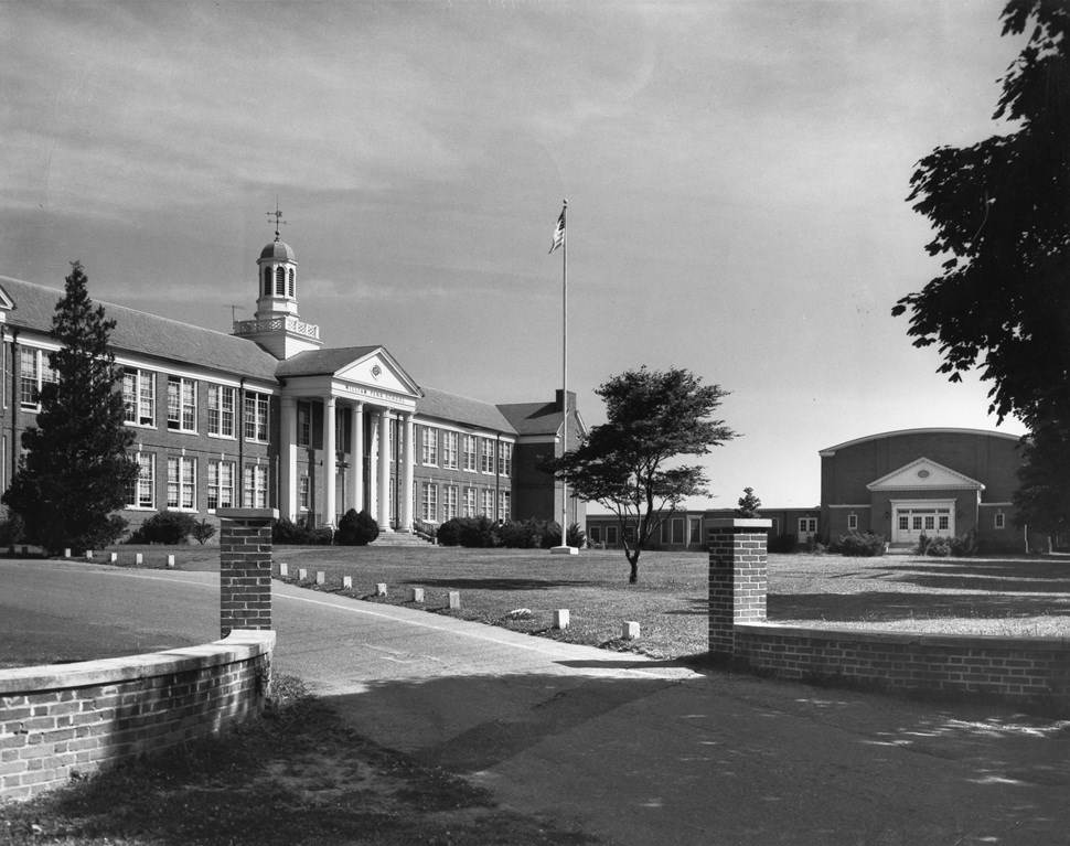 School building with brick walls and a flag pole on the front lawn.
