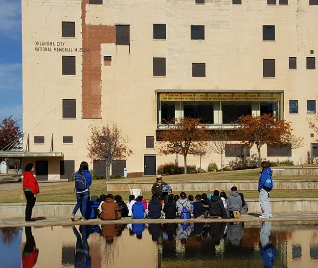 Education Program on the Memorial Grounds Park Ranger sitting in front of children by a reflective body of water