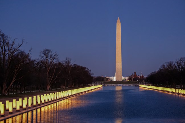 At night, memorial lanterns line the reflecting pool across from the Washington Monument in Washington D.C.