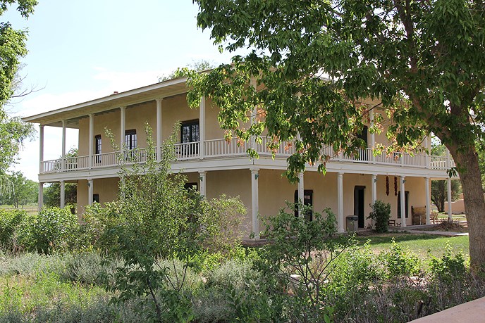 big tan house in background with trees in foreground