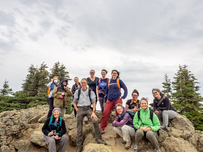 A group of windwept people on a mountain, smiling together