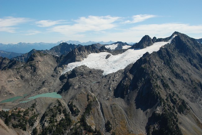 A glacier tucked into the crown of a rocky mountaintop, with a pool of silty tourquiose water below.