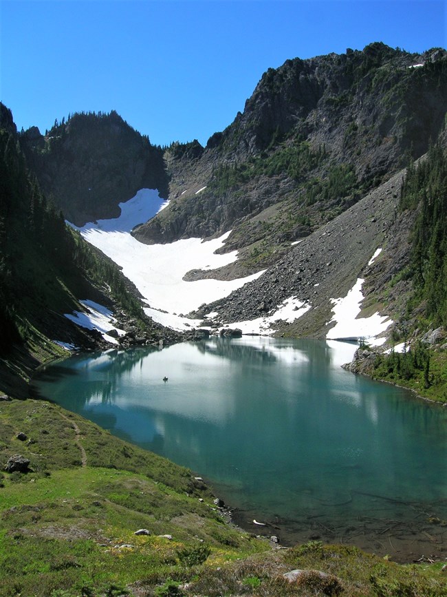 A turquoise mountain lake with glacial ice uphill.