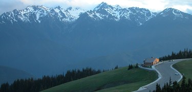 A small building on a hillside, with dramatic mountains beyond.