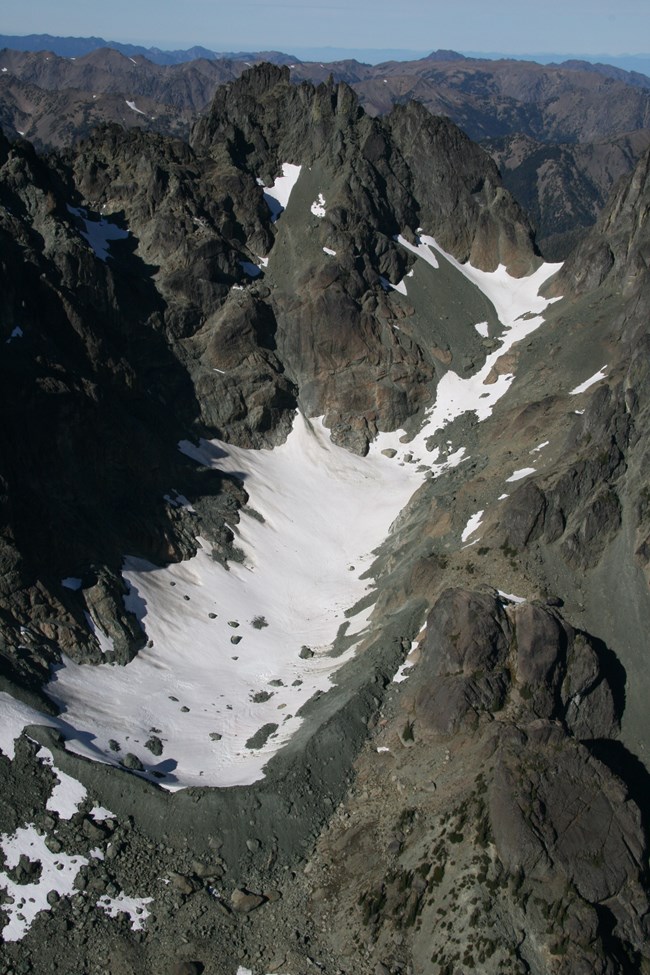 A mountain glacier below a jagged ridge, viewed from above.
