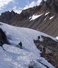 Three climbers navigating a steep slope on a glacier.