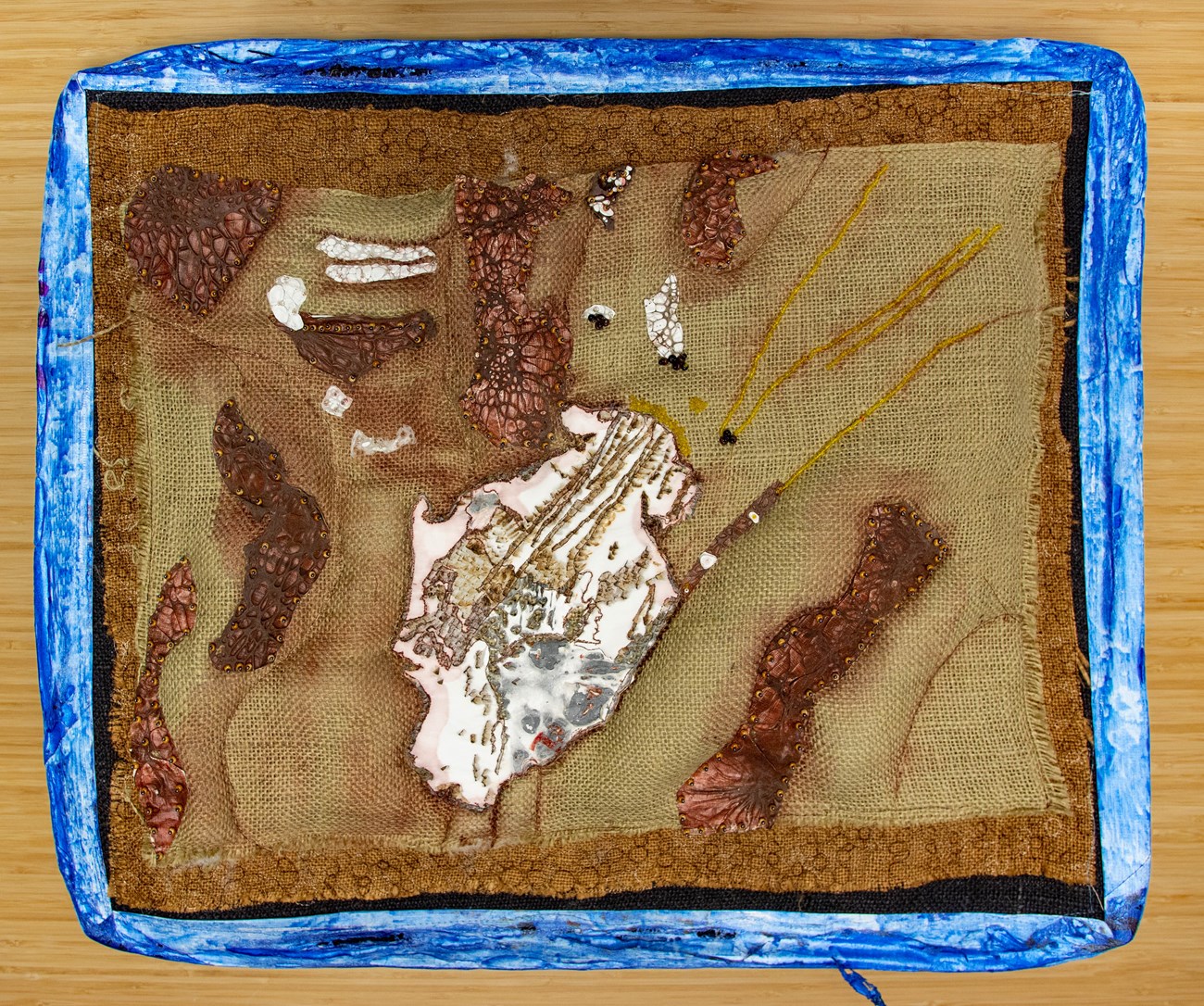 An abstract representation of a mountain glacier made of plastic burlap, and beading, framed in blue tyvec.