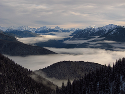 A high vantage of clouds settling in a river valley. Mountain ridges rise above the clouds.