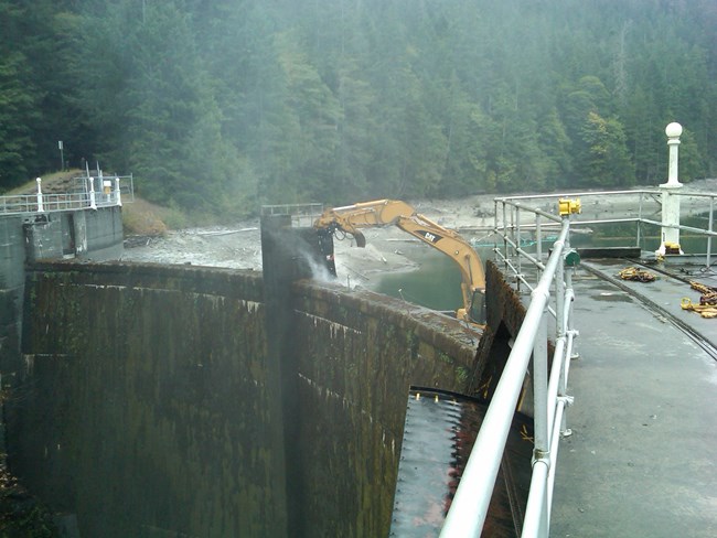 A barge-mounted excavator takes the first chunks of concrete from Glines Canyon Dam.
