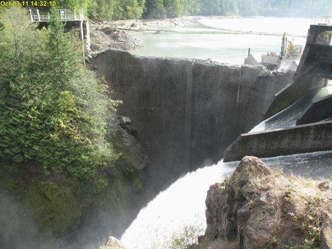 20111003-webcam view of a barge-mounted excavator notching into the upstream face of Glines Canyon Dam.