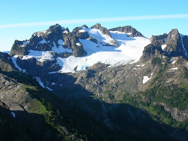 A large glacier clings to the side of a jagged mountaintop.